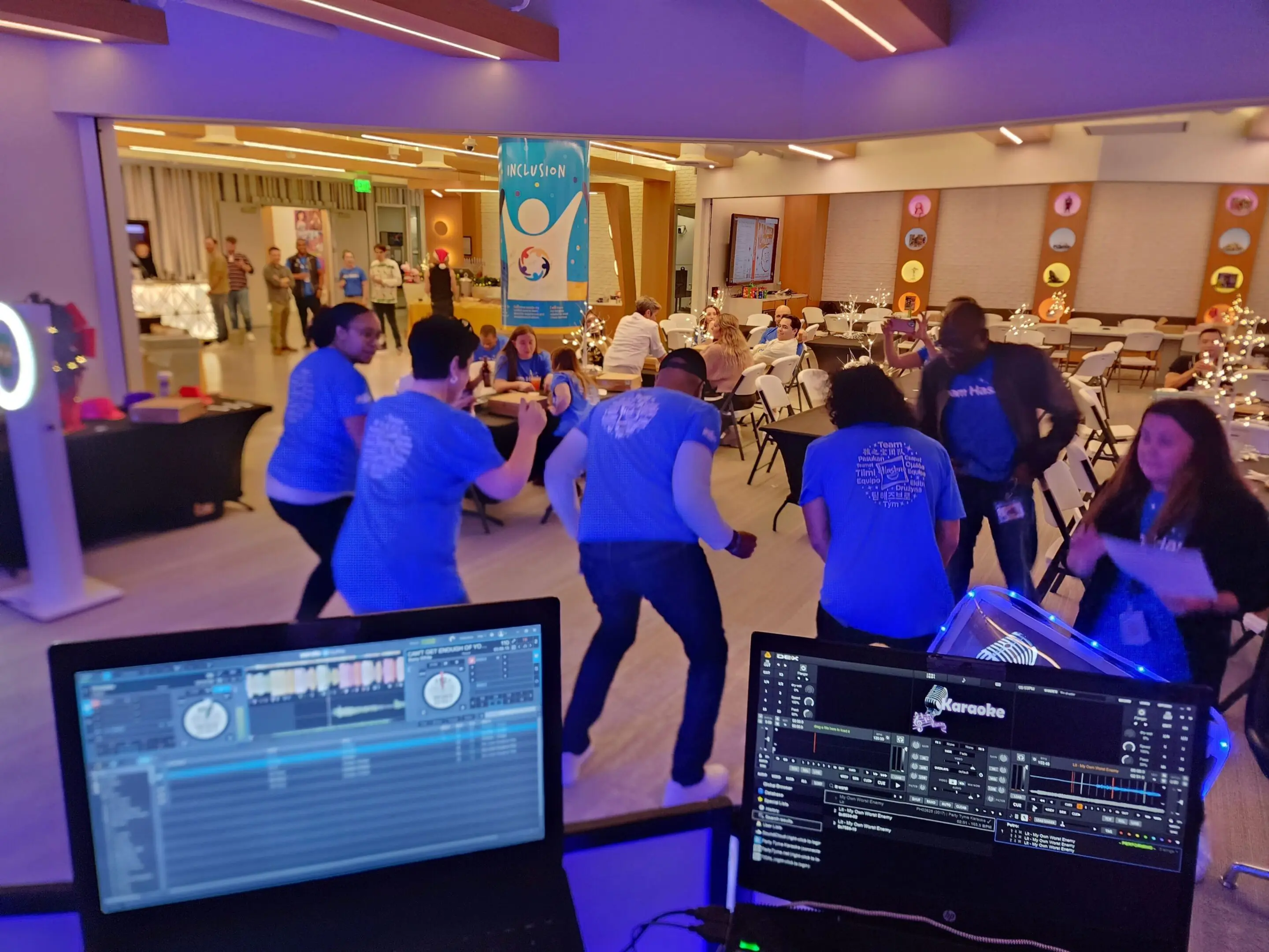 Mr Dj Services event dj services for client Hasbro People dance in a brightly lit room during an indoor event, viewed from behind a DJ station music equipment and the song "wobble"