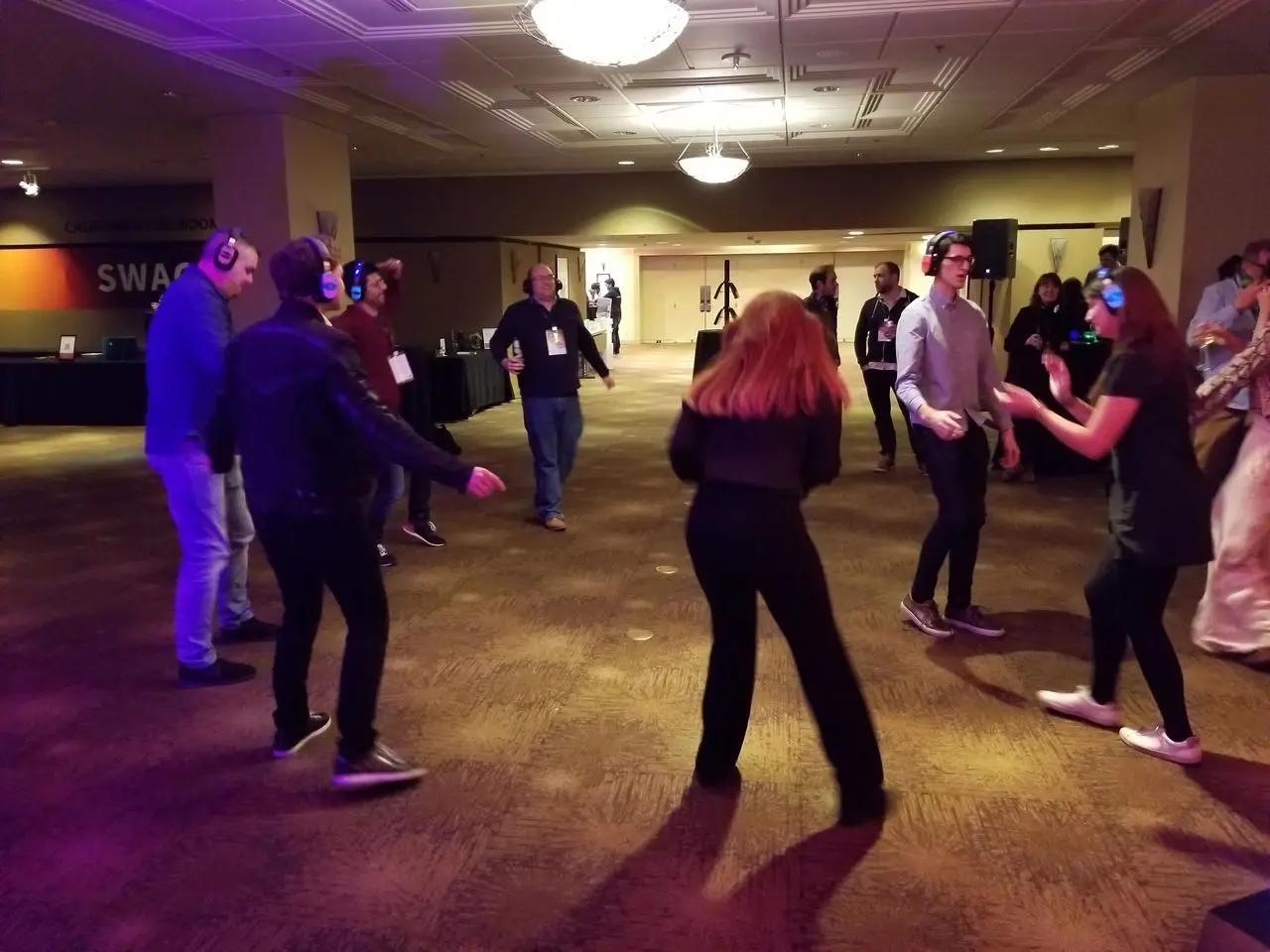 Mr Dj Services People wearing headphones dance in a dimly lit room, participating in a silent disco event. Other attendees stand or watch in the background.