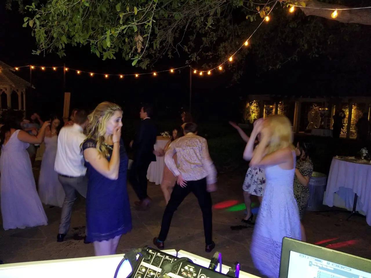 dj services in Los Angeles People dancing outdoors at night under string lights, with DJ equipment visible in the foreground and tables in the background.