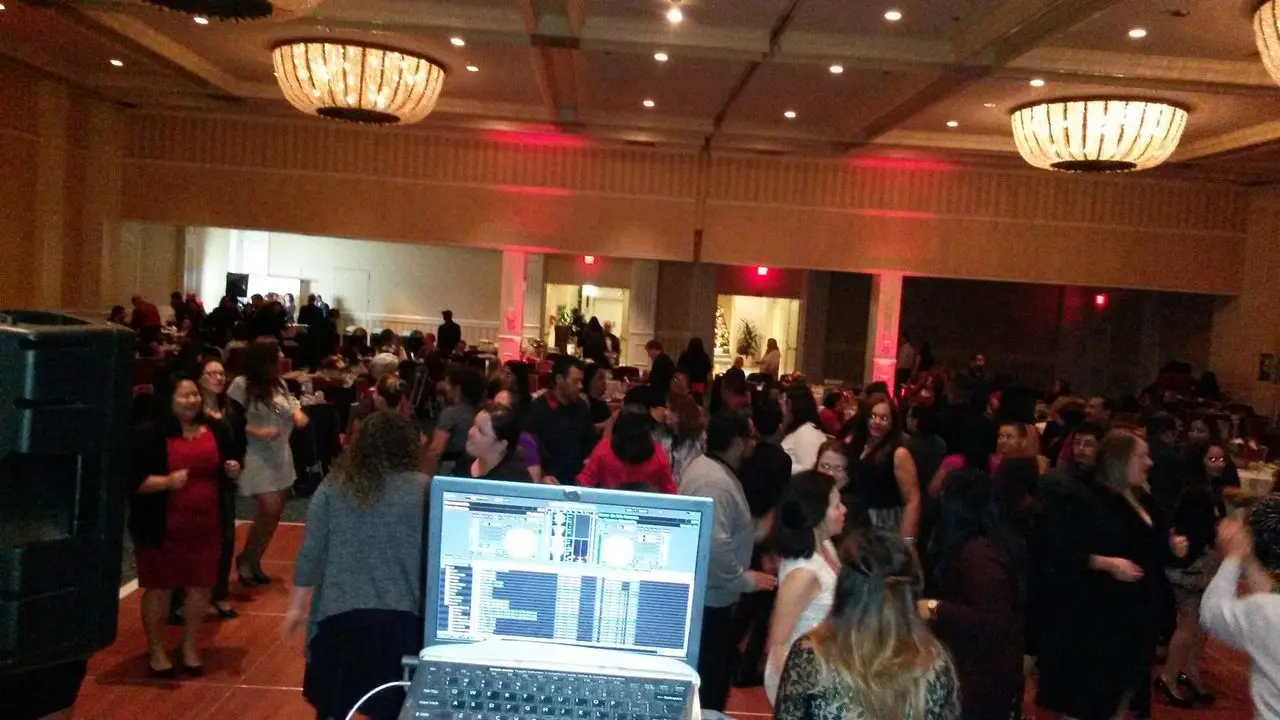 Event Dj Services Large group of people dancing in a ballroom, seen from behind a DJ booth with a laptop displaying mixing software.