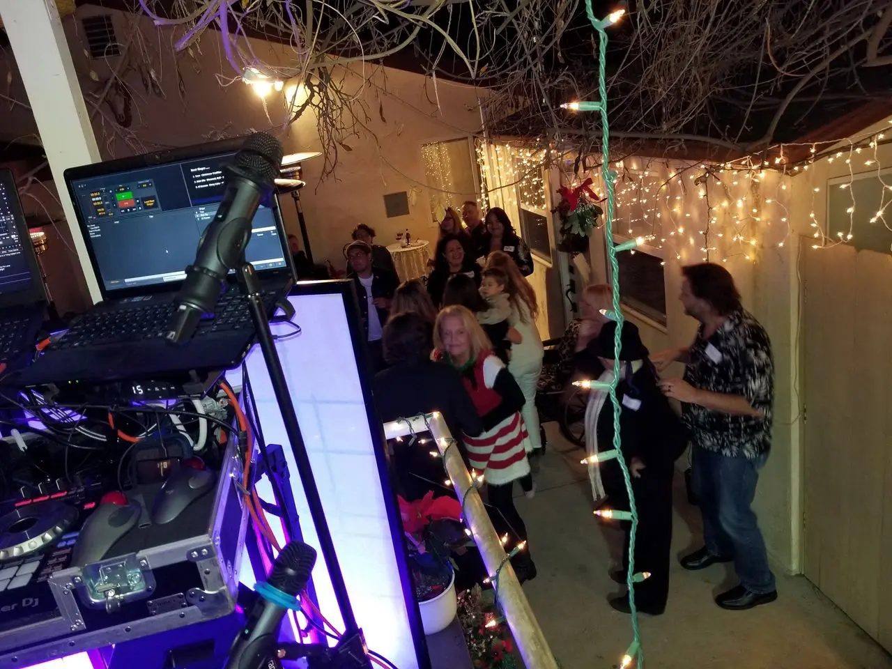 BackYard Boogie - Mr Dj Services A group of people socialize and dance outdoors at night near a DJ booth, surrounded by string lights and festive decorations.