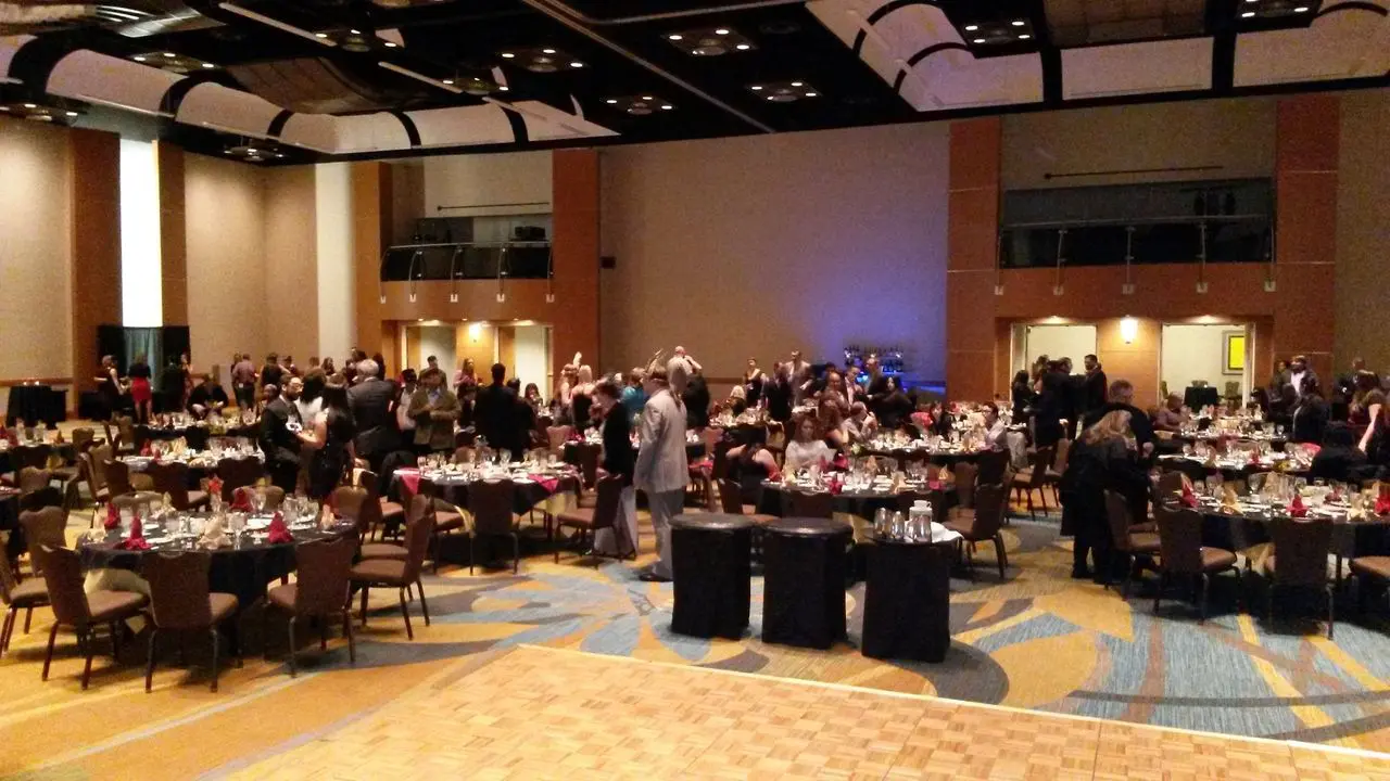 Dj Services - Mr Dj Services People gather and socialize around banquet tables in a large, carpeted event hall with a wooden dance floor in the foreground.