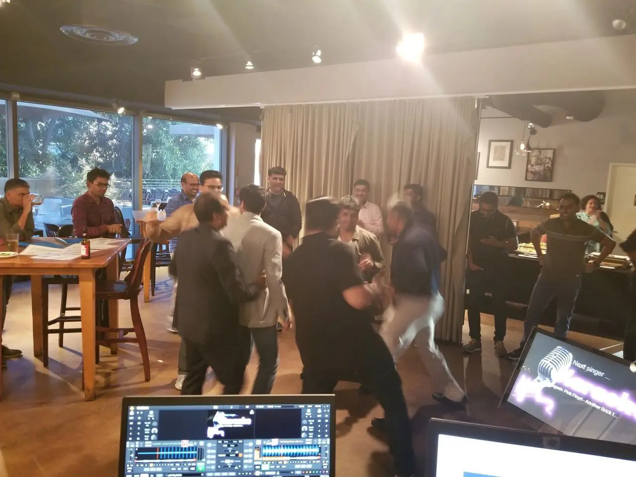 Mr Dj Services Karaoke A group of people are gathered in a restaurant or cafe, some appearing to argue or confront each other while others watch. Tables, chairs, and computer monitors are visible in the foreground.