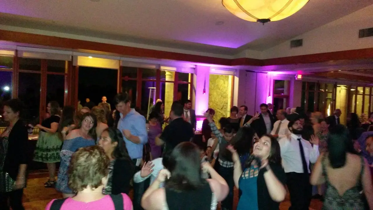 Mr Dj Services Los Angeles A group of people are dancing and socializing in a brightly lit indoor venue with purple accent lighting.