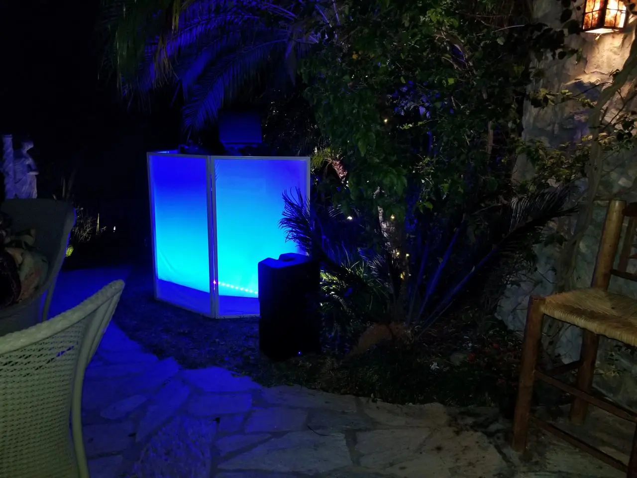 dj services karaoke dj An outdoor scene at night with a glowing blue light panel near tropical plants, a wicker chair, and stone paving visible in the foreground.