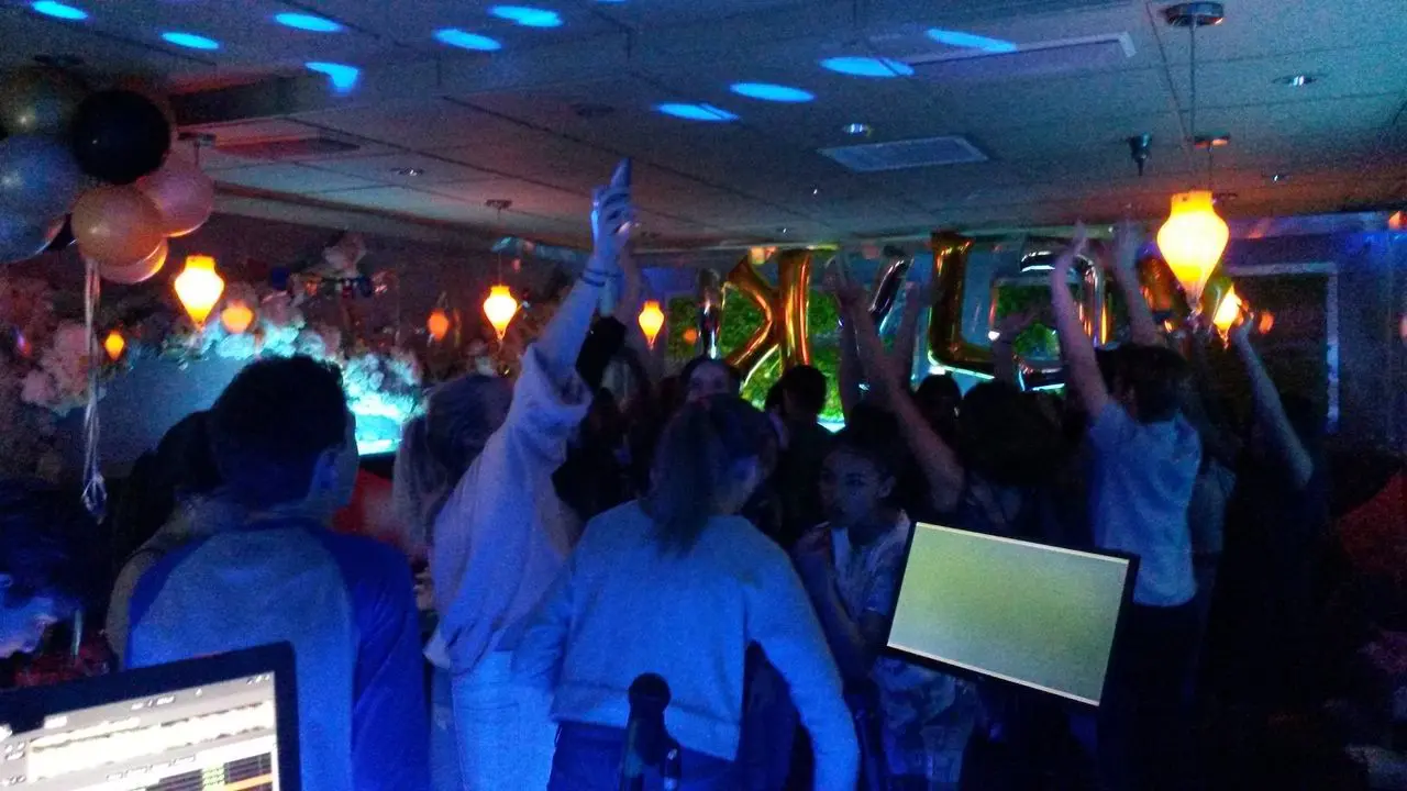 kids karaoke dj Party A group of people dance and raise their arms at a dimly lit party with balloons, decorations, and blue lighting.