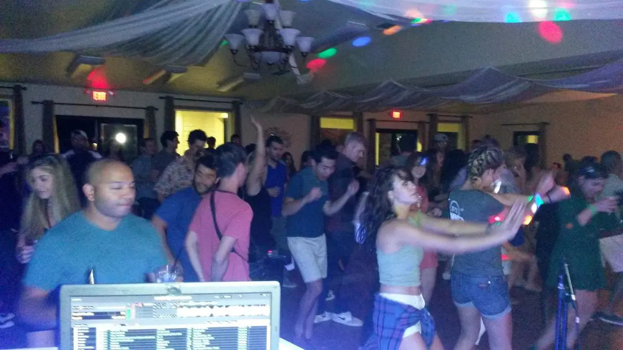 Best Party DJ | Los Angeles Party DJs A crowd of people dance in a dimly lit indoor venue with colorful lights, as a DJ booth is visible in the foreground.