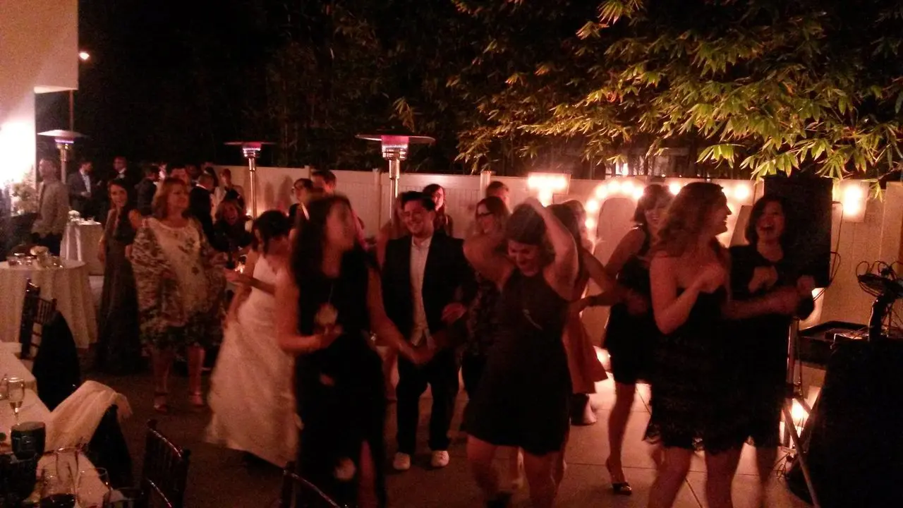 wedding dj services los angeles A group of people dance and socialize at an outdoor evening event, with string lights and patio heaters visible in the background.