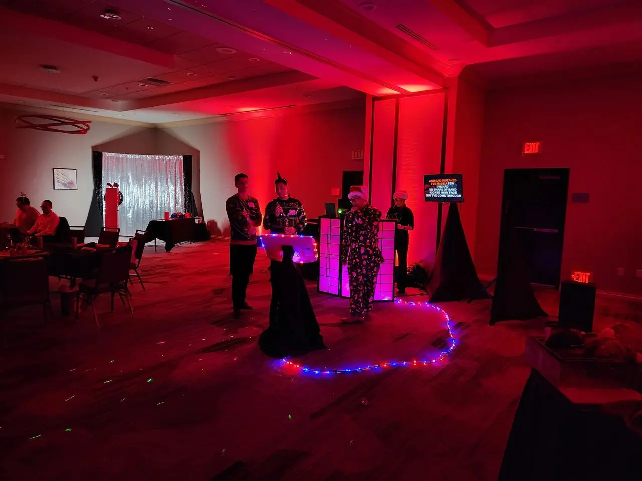 Mr Dj Services karaoke Photo Booth A group of people stands near a DJ booth with colorful lights in a dimly lit room decorated for a party or event.