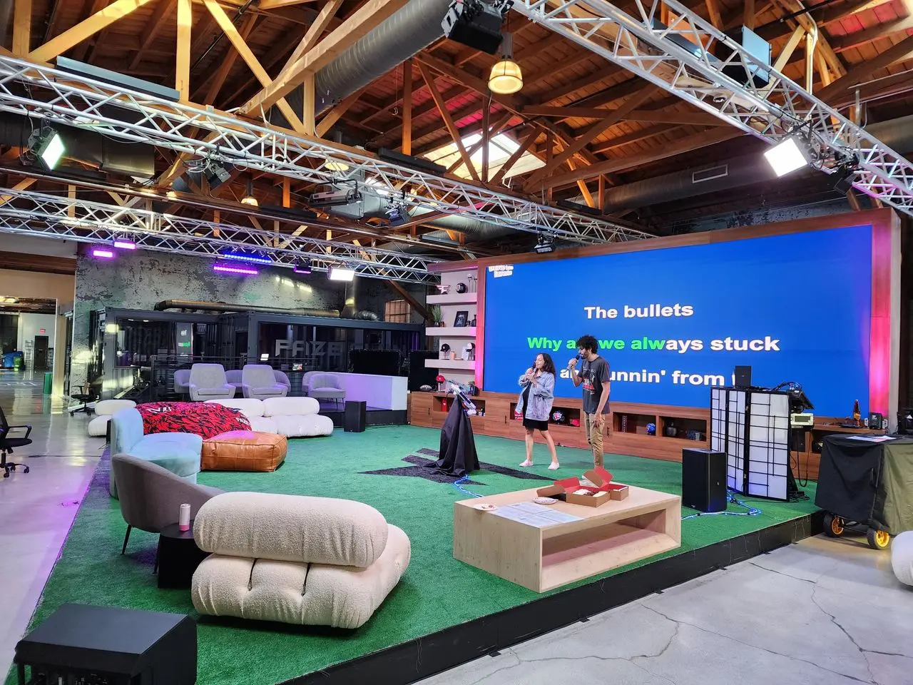 Karaoke Dj corporate Two people stand on a stage with large karaoke lyrics displayed on a screen behind them in a spacious, modern, loft-style room with casual seating and exposed beams.