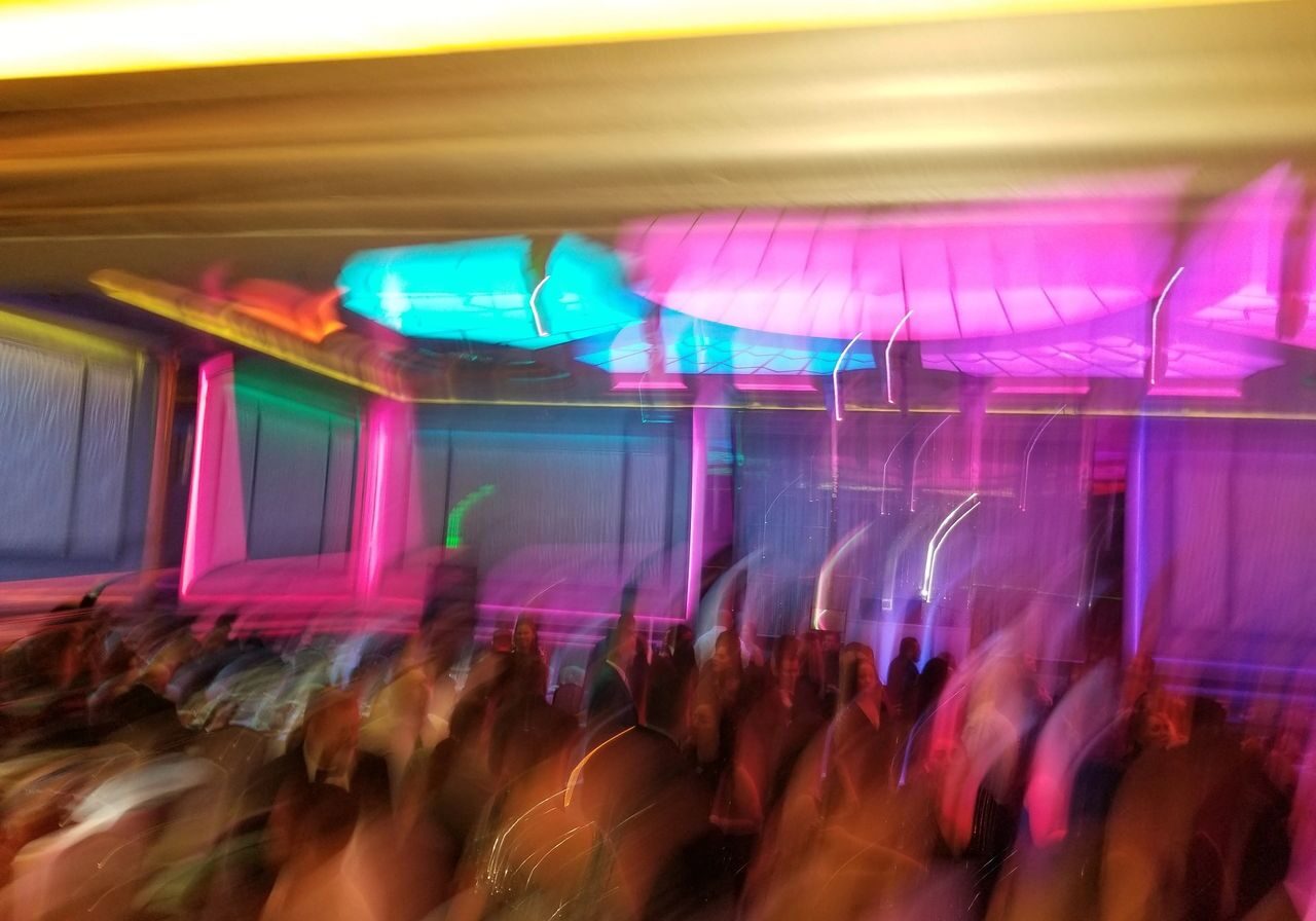 A blurred image shows a crowd under vibrant neon lights in shades of pink, blue, and yellow, creating an abstract effect.