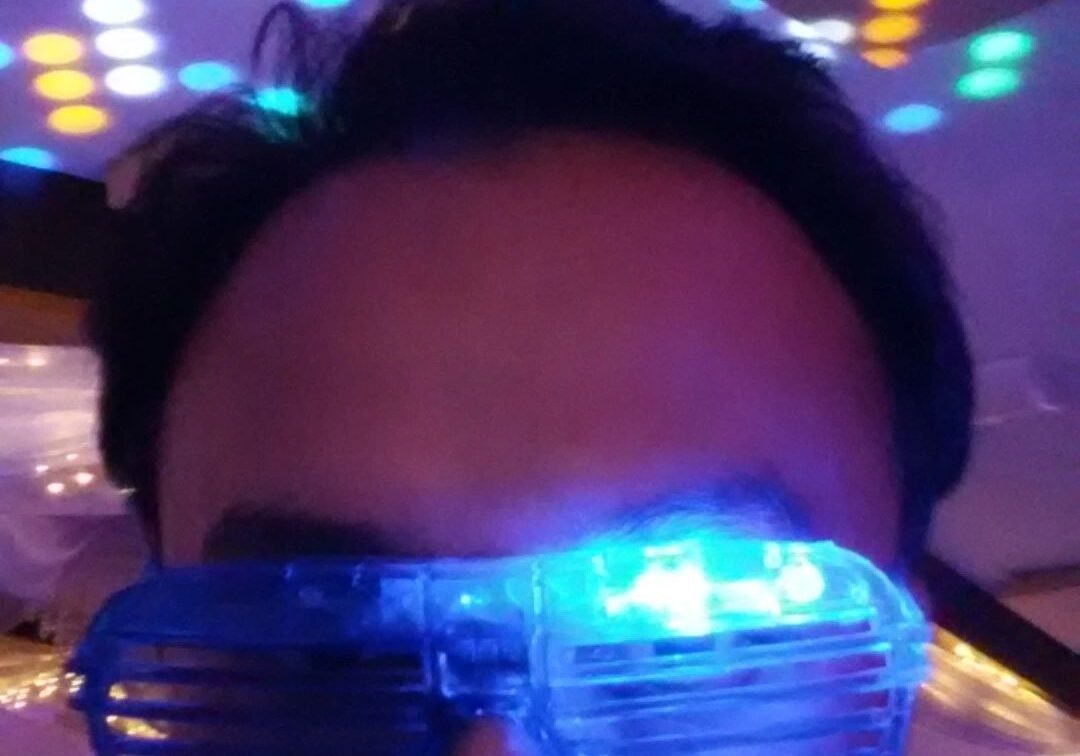 A person wearing blue LED shutter glasses under colorful disco lights with a serious expression.